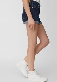 Szorty jeansowe w ciemnym niebieskim kolorze z podwiniętymi krawędziami, posiadające kieszenie z przodu i z tyłu. Do tego białe trampki za kostkę.