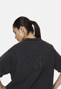 T-shirt nera oversize con maniche corte, caratterizzata da un design a rilievo di farfalla e dalla scritta "GOOD FOR NOTHING" sul retro. Tessuto di cotone morbido.