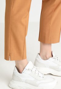 Tan cropped trousers with side slits paired with white athletic sneakers featuring a textured design and thick soles.