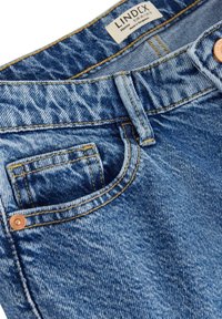Jeans in denim azzurro chiaro con una texture sbiadita, dotati di accessori in rame, cuciture gialle e una tasca porta-monete frontale. Etichetta del brand visibile.