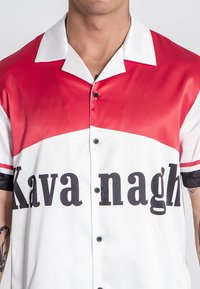 Camisa de botones de manga corta con un diseño de bloques de color rojo y blanco, con el texto negro "Kava nagh" y un acabado suave de satén.