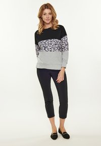 Černá a šedá svršková mikina s leopardím vzorem. Spárováno s úzkými černými kalhotami a černými plochými botami. Hladká struktura látky.