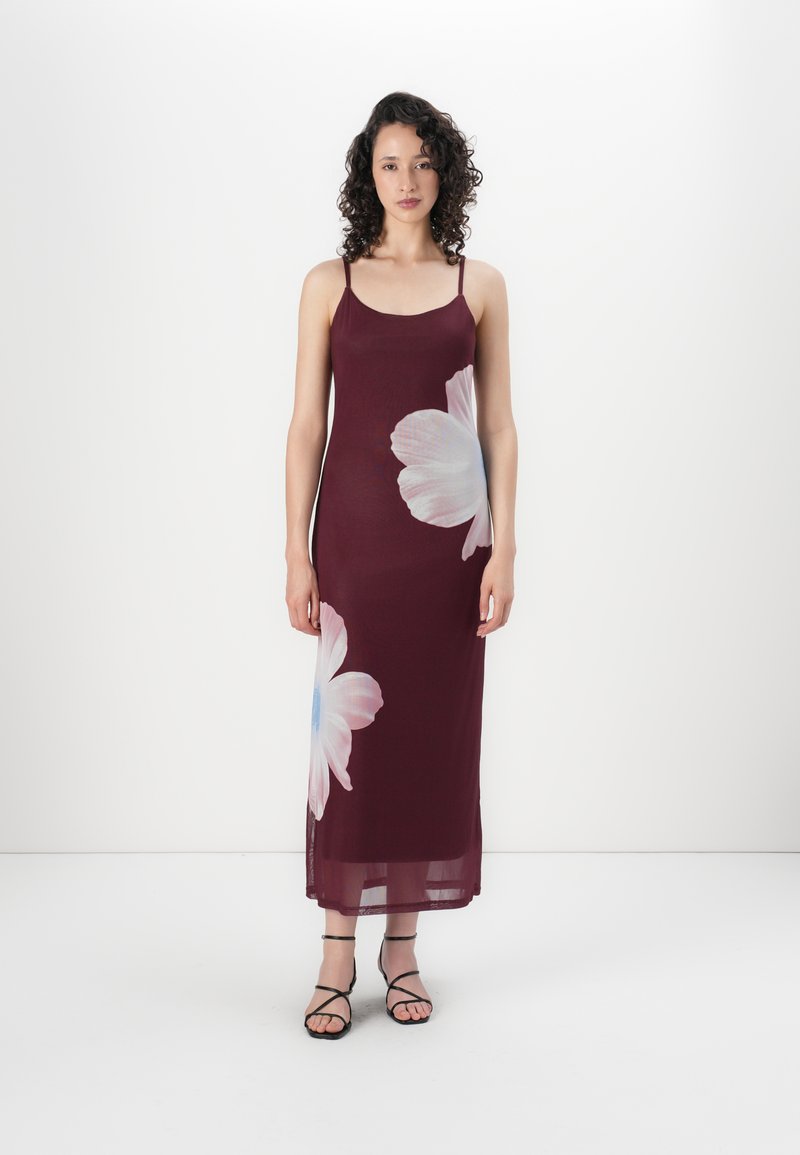 Vestido longo burgundy com alças finas, apresentando uma grande estampa floral branca e um design fluido. Acompanhado por sandálias pretas de tiras.