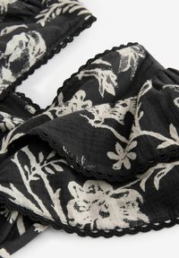 Tessuto nero con motivo floreale bianco, caratterizzato da un bordo in pizzo nero a scallop lungo i lati. Materiale morbido e texturizzato con un design a strati.