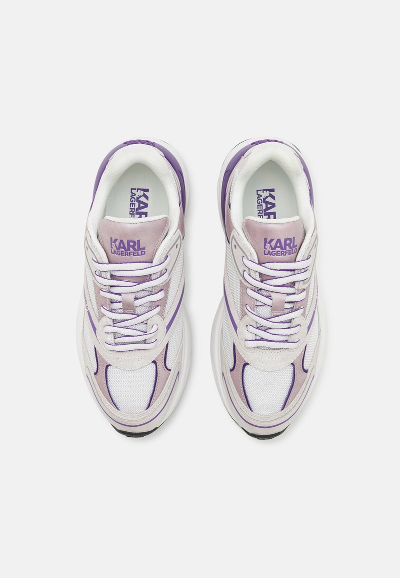 Zapatillas blancas con acentos en lavanda, material de malla, diseño con cordones, puntera redonda y plantillas de marca. Presenta líneas curvas y un cuello acolchado.