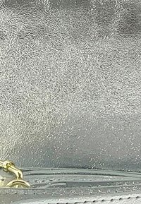 Zilverkleurig leren oppervlak met een glanzende afwerking. Bevat gouden hardware en een subtiel nerfpatroon, wat de hoogwaardige afwerking toont.