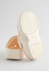 Krém színű papucsok sima műanyag külsővel, nyitott háttal és mintás talppal. Tartalmaznak szellőzőnyílásokat és "14.0" méretjelzést.