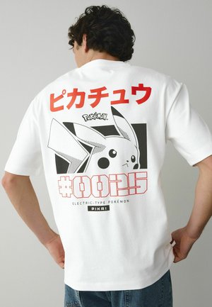 Mann trägt ein weißes T-Shirt mit großem schwarz-weißem Pikachu-Print und rotem japanischem Text auf der Rückseite, kombiniert mit blauen Jeans.