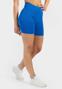 Pantaloni corti sportivi blu con vita alta, realizzati in tessuto elasticizzato. Presentano una texture liscia e dettagli di cucitura sottili. Abbinati a sneaker bianche.
