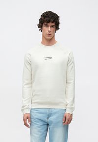 Vaaleanbeige collegepaita pyöreällä pääntiellä ja raglan-hihoilla. Edessä pieni painettu logo rinnassa. Pehmeä kangas ja rento istuvuus.