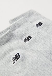 Graue Socken mit einer weichen Textur, die ein schwarzes gesticktes Logo zeigen. Drei Paare sind sichtbar und präsentieren ein geripptes Bündchen-Design.