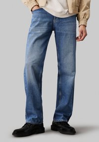 Jeans din denim de culoare albastru deschis, cu croială dreaptă, având un finisaj decolorat și un design standard cu cinci buzunare. Purtați cu pantofi negri.
