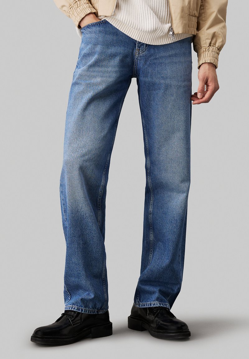Jeans din denim de culoare albastru deschis, cu croială dreaptă, având un finisaj decolorat și un design standard cu cinci buzunare. Purtați cu pantofi negri.