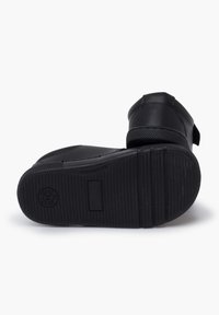 Chaussure noire pour enfants avec semelle en caoutchouc texturé, bande auto-agrippante et marquage "Hecho en España" sur la semelle, présentée sur un fond blanc.