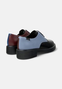 Paire de chaussures à lacets en cuir bicolore avec semelles épaisses noires, présentant des accents de talon bleu clair, noir, bordeaux et bleu.