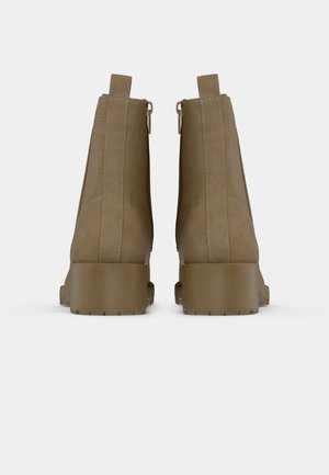 Paar braune Wildleder-Stiefeletten mit dicken Absätzen und Zuglaschen, von hinten vor weißem Hintergrund gesehen.