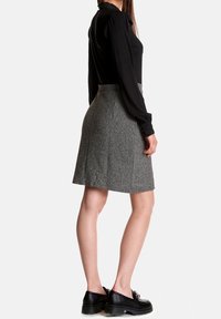 Gonna in tweed grigia con design svasato, caratterizzata da vita alta e pieghe, abbinata a una blusa nera a maniche lunghe e scarpe con piattaforma nere.