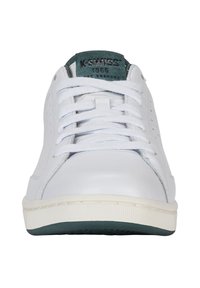 Sneakers din piele albă cu un design perforat, sistem de închidere cu șireturi, limbă din suede verde și o talpă intermediară albă căptușită. Talpa din cauciuc vizibilă la baza acestora.
