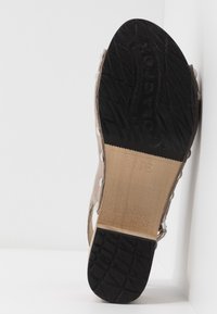 Sandale beige avec tige en daim, dotée d'une semelle en caoutchouc noir texturé, d'un intercalaire en bois et d'accents en métal argenté le long des sangles.