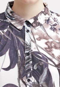 Floral-patterned shirt with a collared neckline, featuring dark buttons and a smooth fabric texture in shades of purple and white.