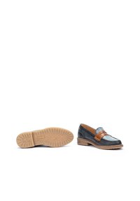 Mocasines de cuero negro con una correa de cuero marrón, puntera redonda y suela de goma texturada. Detalle de costura lateral y tacón bajo apilado.