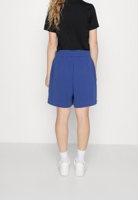 Modré, šortky po kolena s elastickým pasem. Materiál vypadá měkce a mírně strukturovaně. Spárované s černým tričkem a bílými teniskami.