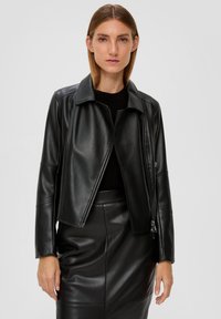 Veste en cuir noir avec un col, fermeture éclair et manches longues. Texture lisse, design court, associée à une jupe assortie.