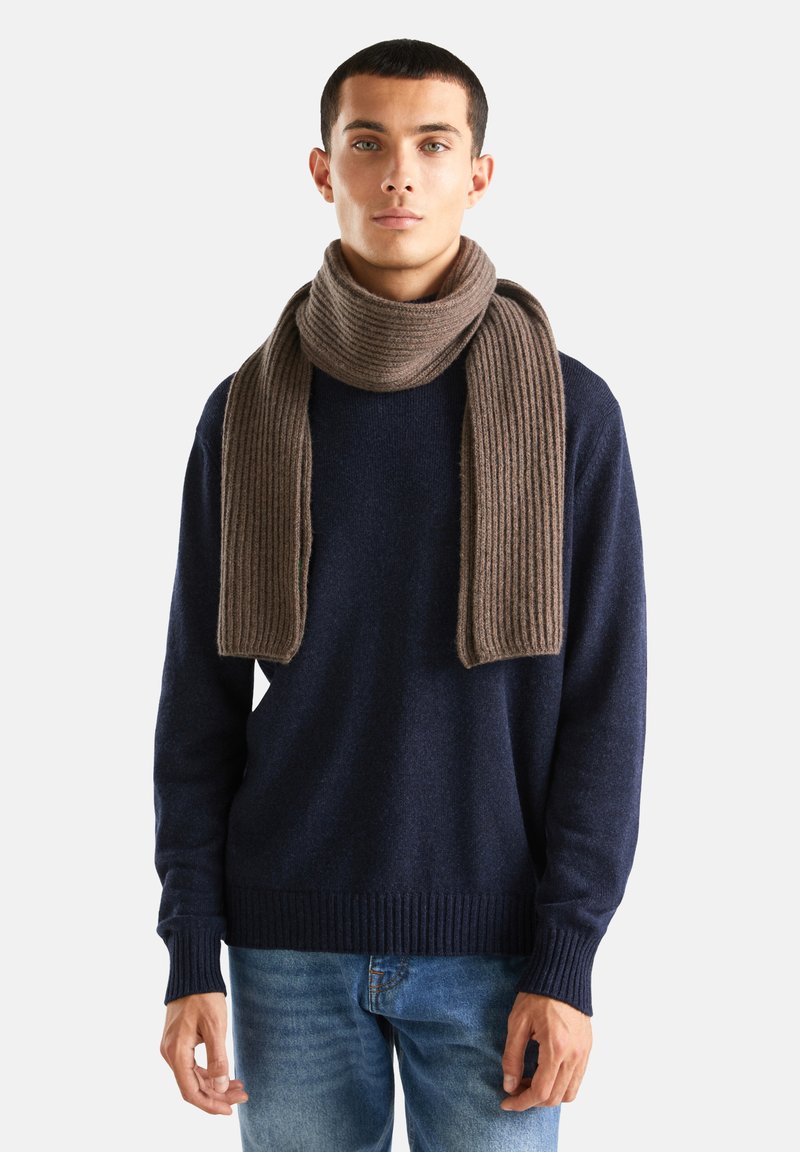 Bruine geribde sjaal om de hals gewikkeld, gecombineerd met een donkerblauwe gebreide trui. Casual blauwe jeans zichtbaar. Zachte textuur, warme uitstraling.