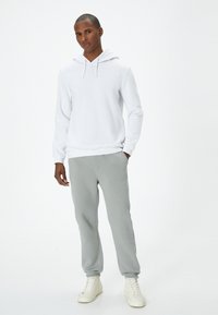Witte hoodie met een trekkoord, gecombineerd met lichtgrijze joggingbroek met elastische boorden, gedragen met witte hoge sneakers.