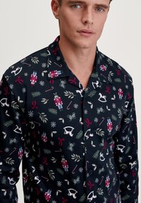 Navyblaues Button-Up-Shirt mit festlichem Print, der Nussknacker, Zuckerstangen und Feiertagsmotive zeigt. Weicher Stoff mit einem entspannten Kragen und Schnitt.