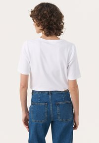 Hvid kortærmet t-shirt med rund halsudskæring, parret med højtaljede blå denimjeans med to baglommer og en afslappet pasform.