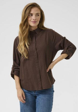 Brown button-up shirt made of lightweight fabric, featuring a collar, rolled sleeves, and a relaxed fit. Paired with blue jeans.