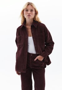 Bourgogne korduroy-skjorta med två bröstfickor och knäppning, tillsammans med matchande byxor. Slät textur och lös passform.