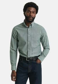 Groen-witte gestreepte button-up shirt met een zak, gecombineerd met donkere denim jeans en een zwarte gevlochten riem.