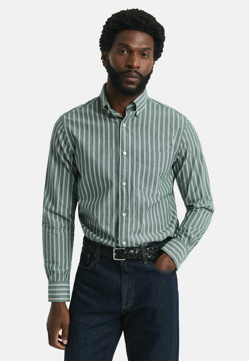 Groen-witte gestreepte button-up shirt met een zak, gecombineerd met donkere denim jeans en een zwarte gevlochten riem.