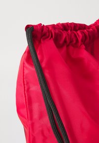 Rød nylon pose med snor og sort snor. Har en glat overflade og et enkelt, funktionelt design.