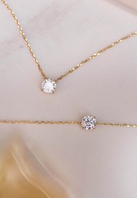 Goldkette und Armband mit runden, klaren Kristallen, die in sechs-Prong-Einstellungen gefasst sind, auf einer hellen Oberfläche präsentiert.
