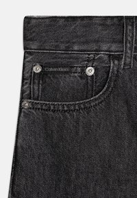 Mustad denim püksid klassikalise lõikega, väike esikott, hõbedased metalldetailid ning Calvin Kleini silt vööl.