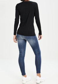 Black long-sleeve top, fitted design, smooth texture. Paired with blue skinny jeans, medium wash, slight distressed detailing at hem. White sneakers.