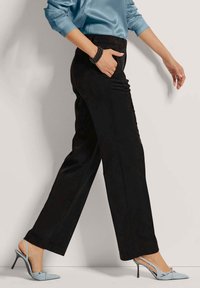 Zwarte wijde broek met een gladde textuur en een elastische tailleband, gecombineerd met lichtblauwe puntige hakken en een satijnen blauwe top.