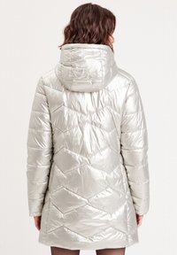 Chaqueta de puff plateada con capucha, patrón de acolchado en forma de chevrón, textura brillante y diseño de longitud media. Fabricación ligera e aislante.