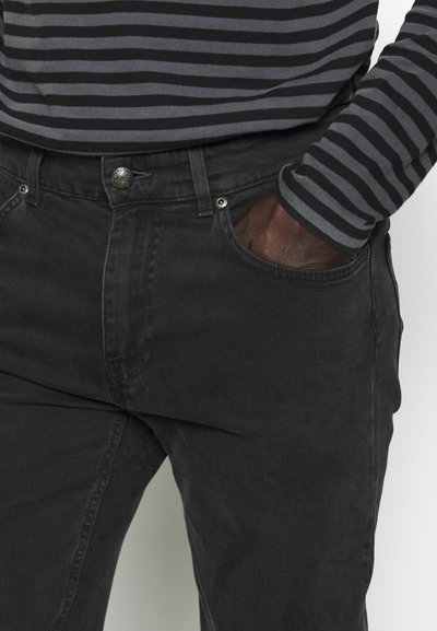 Jean noir en denim au design classique, avec un bouton en métal et des poches avant. Porté avec une chemise à rayures noire et grise à manches longues.