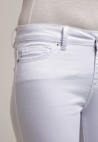 Jeans de mezclilla blanca con un diseño clásico de cinco bolsillos, con detalles de costura sutiles y herrajes metálicos en la cinturilla.