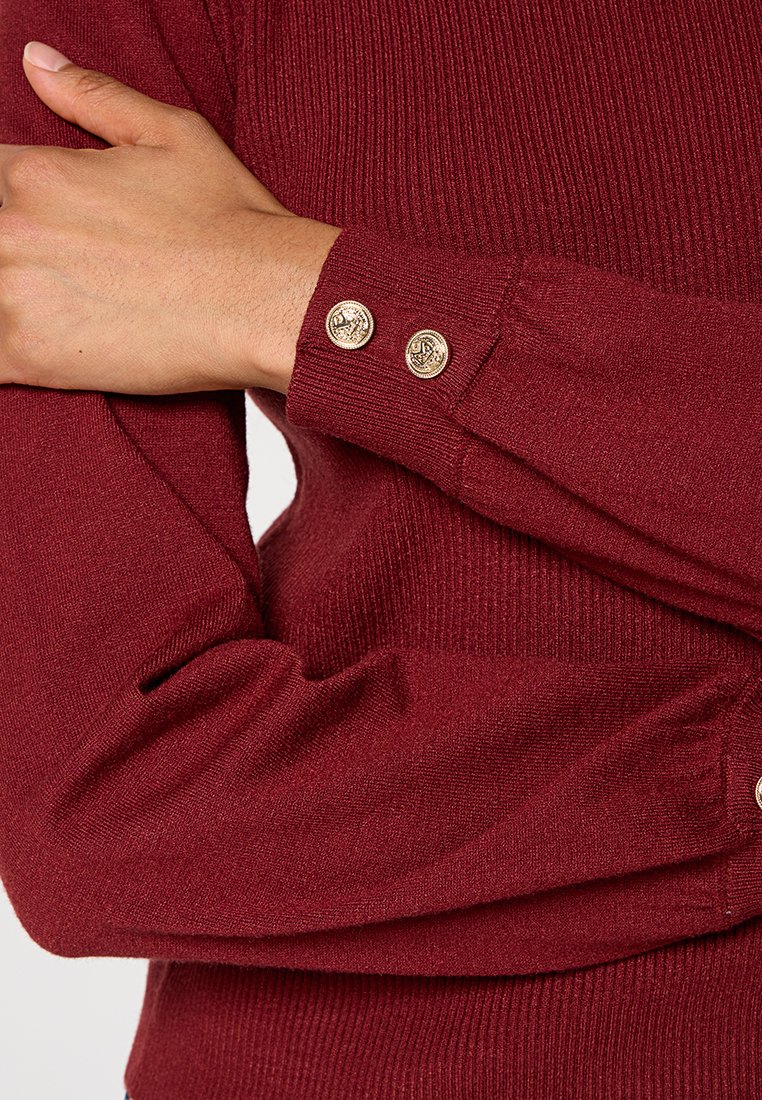 Bordeaux trui met ribbeltextuur, met een aansluitende pasvorm en gouden knoopaccenten op de manchetten.