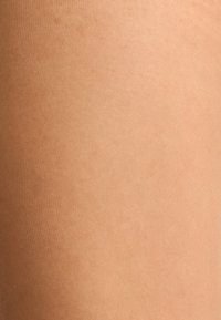 Durchsichtige hautfarbene Strumpfhosen mit glatter Textur und geripptem Muster, die in einem hellbraunen Farbton gehalten sind und sich für verschiedene Hauttöne eignen.