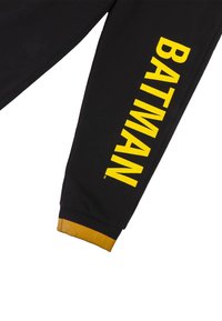 Zwarte sweatpants met gele "BATMAN" tekst verticaal aan de zijkant bedrukt. Voorzien van een geribbelde gele boord aan de onderkant van het been.
