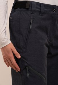 Pantaloni tehnici de culoare gri închis, cu buzunare cu fermoar, talie ajustabilă și o textură netedă. Prezintă cusături întărite și un design pe panouri.