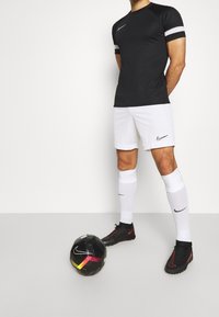 Svart Nike träningströja med vita och grå randiga ärmar, matchad med vita shorts, svarta fotbollsskor och en svart fotboll.