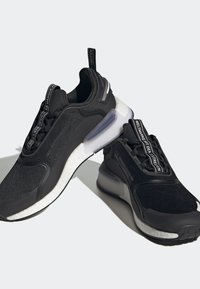 Ett par svarta träningssneakers med vita dämpade sulor och märkta dragflikarna, uppvisade på en ljus bakgrund med mjuka skuggor.