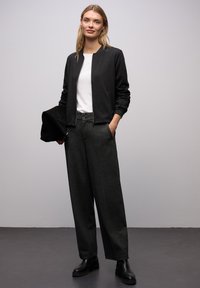 Černá bomber bunda, bílé tričko, šedé široké kalhoty, černé kotníkové boty. Hladká textura s pohodlným střihem, s předním zipem a kapsami.